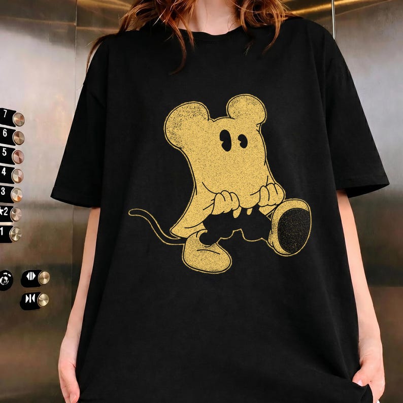 May include: Black t-shirt featuring a vintage-style cartoon mouse character in gold. The mouse is depicted in a seated position with large ears and a long tail. The graphic is centered on the front of the shirt.