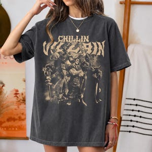 May include: A charcoal gray short-sleeve t-shirt featuring a distressed beige graphic print of various animated villains. The text "CHILLIN Like a VILLAIN" is printed in a stylized font above the characters. The shirt has a crew neckline.