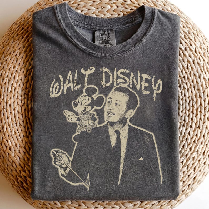 May include: Dark gray t-shirt featuring a vintage-style graphic of Walt Disney with Mickey Mouse. The text "WALT DISNEY" is arched above the illustration. The shirt has a crew neck and a Comfort Colors tag.