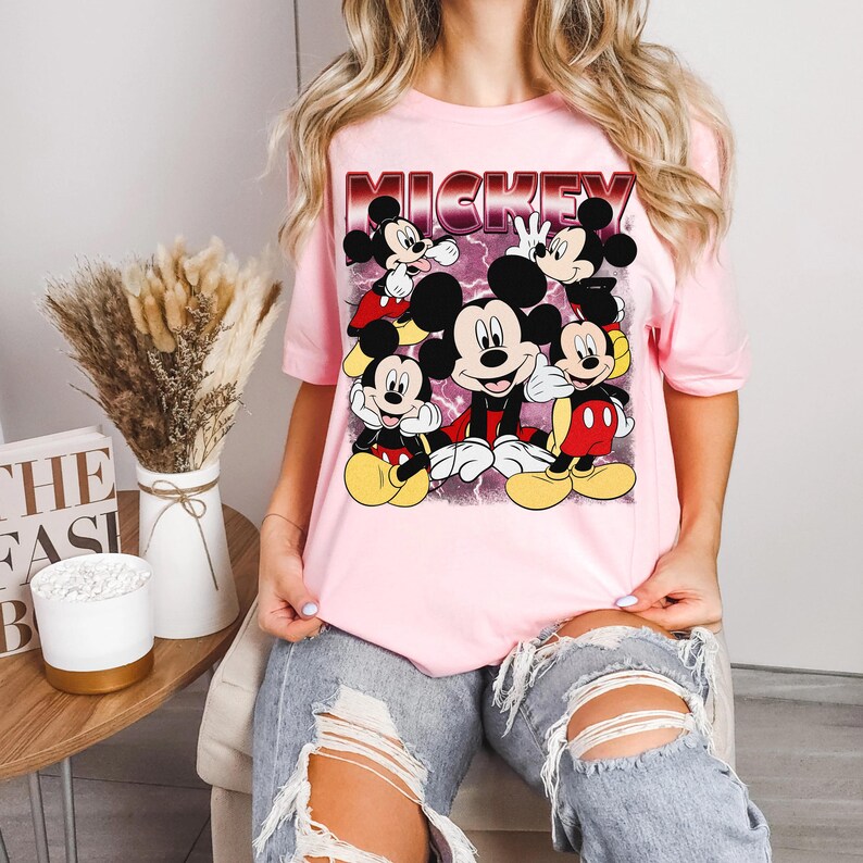 Puede incluir: Camiseta rosa claro con un dise&ntilde;o de Mickey Mouse en varias poses y la palabra "MICKEY" en una fuente retro roja y blanca. La camiseta es de manga corta y tiene cuello redondo.