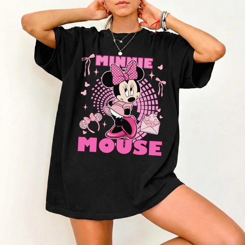 May include: Black t-shirt with a Minnie Mouse graphic. The design features Minnie Mouse in pink, a pink bow, and the words "MINNIE MOUSE" in pink. Pink hearts and bows are also included in the design.
