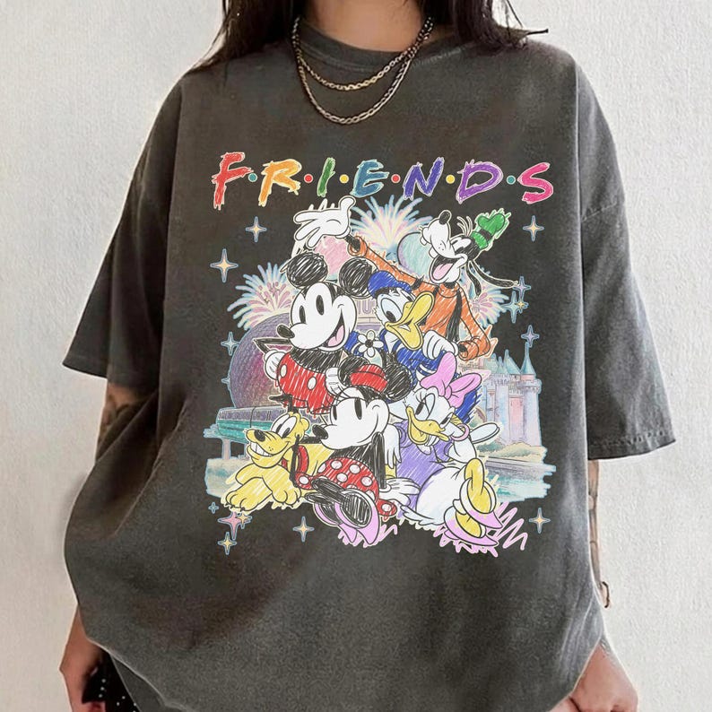 May include: Dark gray t-shirt featuring the word "FRIENDS" in colorful lettering above a graphic of Disney characters including Mickey Mouse, Minnie Mouse, Donald Duck, and Goofy. The design includes fireworks and a castle.