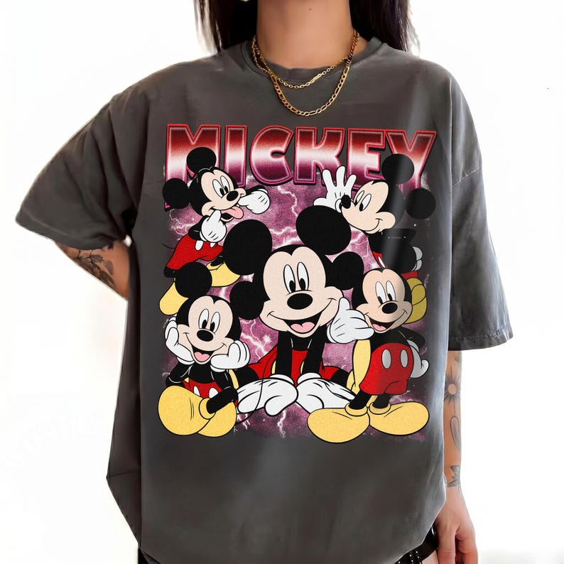 Puede incluir: Camiseta gris con un dise&ntilde;o de Mickey Mouse en varias poses. La palabra "MICKEY" est&aacute; impresa en rojo y rosa en la parte superior. Mickey lleva pantalones cortos rojos y zapatos amarillos. Una prenda casual.