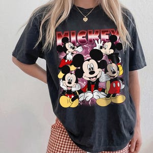 Puede incluir: Camiseta negra con un dise&ntilde;o de Mickey Mouse en varias poses. La palabra "MICKEY" est&aacute; impresa en rojo y blanco. La camiseta tiene un aspecto vintage y descolorido.