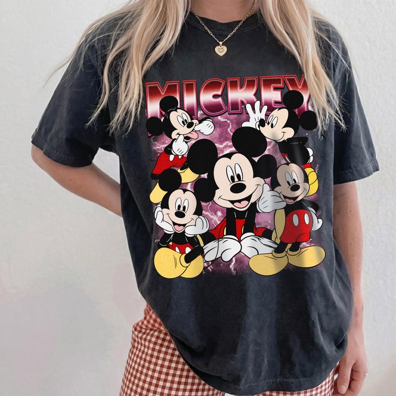 Puede incluir: Camiseta negra con un dise&ntilde;o de Mickey Mouse en varias poses. La palabra "MICKEY" est&aacute; impresa en rojo y blanco. La camiseta tiene un aspecto vintage y descolorido.