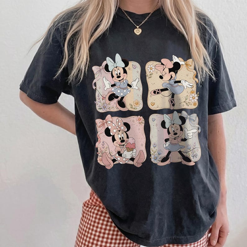 May include: Black t-shirt featuring four square illustrations of Minnie Mouse in various poses. Each image has a floral background and a pastel color scheme. The shirt is a relaxed fit.