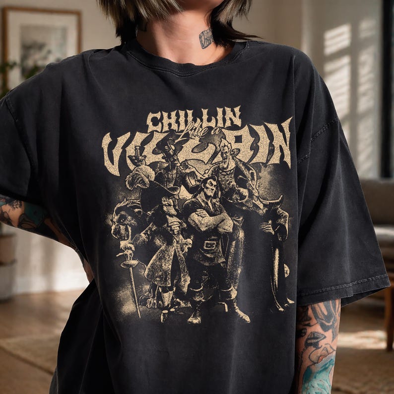 May include: A charcoal black short-sleeve t-shirt featuring a distressed beige graphic print of various animated villains. The text "CHILLIN Like a VILLAIN" is printed in a bold, stylized font above the group of characters on the front of the shirt.