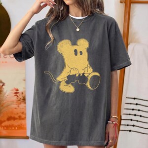 May include: Dark grey t-shirt featuring a yellow cartoon mouse design. The mouse is sitting with its hands clasped and has a long tail. The shirt has short sleeves and a relaxed fit, suitable for casual wear.