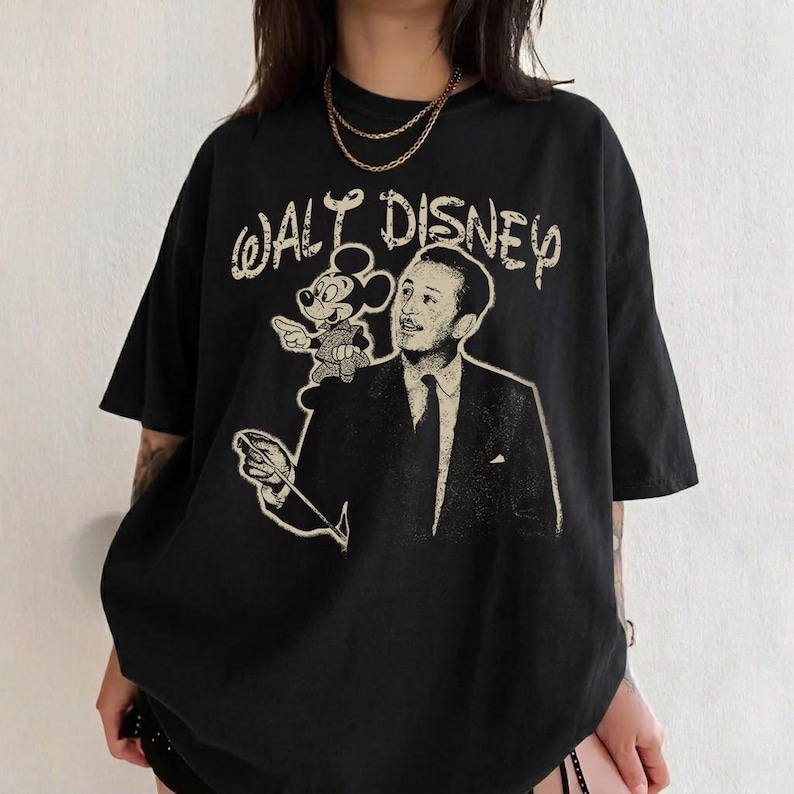 May include: Black t-shirt featuring a vintage graphic of Walt Disney with Mickey Mouse and the text "WALT DISNEY" in a distressed font. The shirt has short sleeves and a relaxed fit.