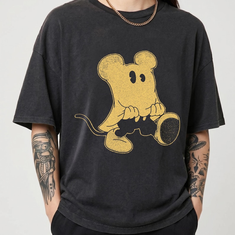 May include: Dark gray t-shirt featuring a distressed yellow cartoon mouse character. The mouse is sitting and holding a large, round object. The shirt has short sleeves and a crew neck.
