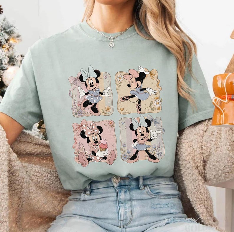 May include: A light green t-shirt featuring four square illustrations of Minnie Mouse in various poses. Each illustration has a different background color and floral accents. Minnie Mouse is wearing different outfits and bows in each illustration.