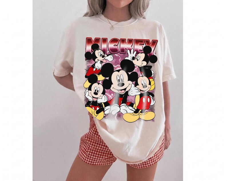 Puede incluir: Camiseta color crema con un gr&aacute;fico de Mickey Mouse en varias poses. La palabra "MICKEY" est&aacute; impresa en una fuente degradada roja y morada en la parte superior. La camiseta se combina con pantalones cortos a cuadros rojos y blancos.