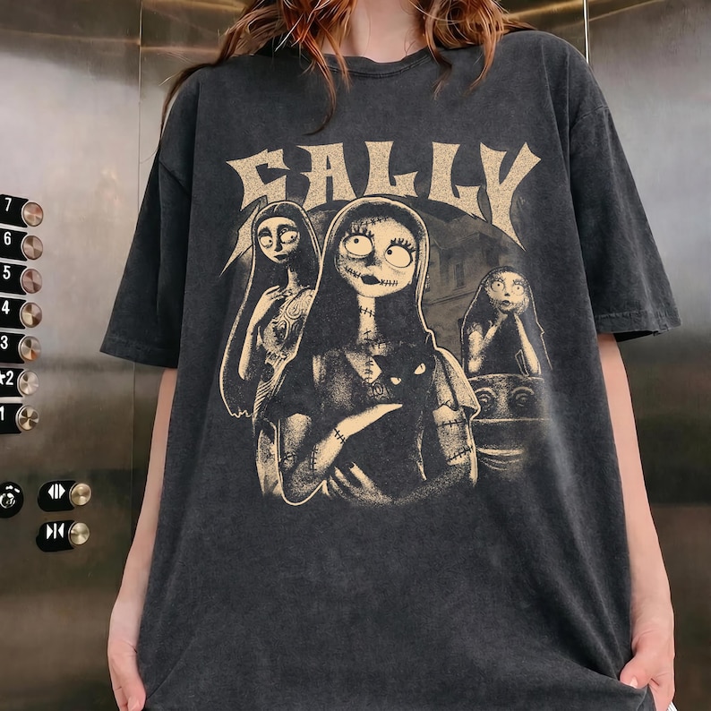May include: A charcoal gray short-sleeve t-shirt featuring a distressed graphic print of the character Sally from The Nightmare Before Christmas. The design includes the text SALLY in a large, stylized font above three illustrations of the character.