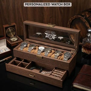 May include: A wooden watch box with a glass top, displaying six wristwatches on tan cushions. The box has a pull-out drawer with compartments for jewelry. The text "PERSONALIZED WATCH BOX" is at the top.