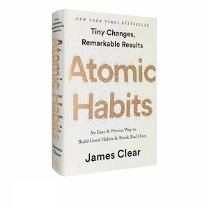 May include: A hardcover book titled "Atomic Habits" by James Clear. The cover is white with gold lettering and the text "Tiny Changes, Remarkable Results." The book's spine also displays the title.