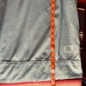 May include: A light blue fabric is measured with an orange measuring tape. The tape shows measurements from 18 to 31 inches. The fabric has a seam at the 28-inch mark. The fabric is slightly wrinkled.