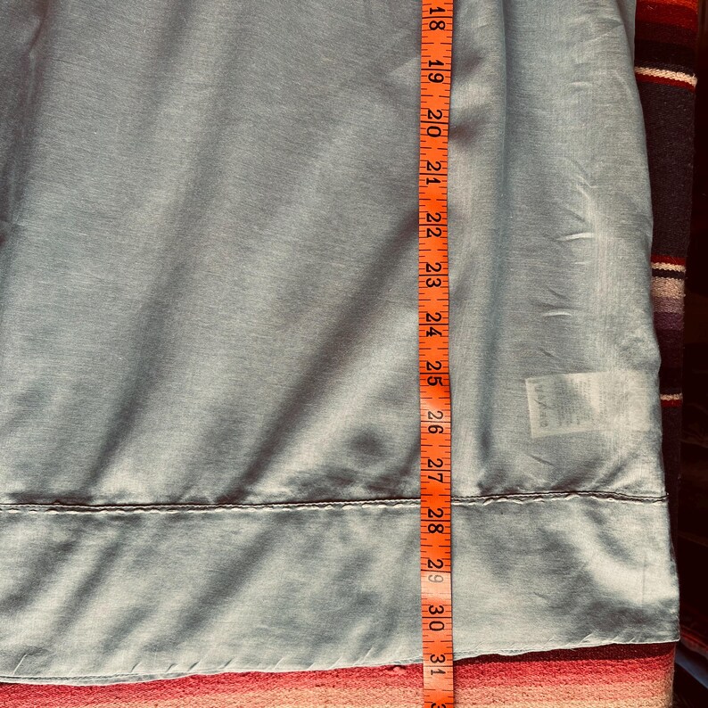 May include: A light blue fabric is measured with an orange measuring tape. The tape shows measurements from 18 to 31 inches. The fabric has a seam at the 28-inch mark. The fabric is slightly wrinkled.