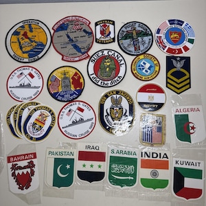 Może przedstawiać: Kolekcja haftowanych naszywek wojskowych i naklejek z flagami o różnych wzorach, w tym Operation Desert Shield, USS Thomas S. Gates, Suez Canal, Vietnam Veteran oraz flagi narodowe krajów takich jak Bahrajn, Pakistan, Irak i Kuwejt.