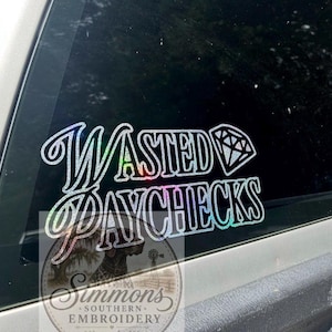 May include: A holographic sticker with the words "WASTED PAYCHECKS" in a script font, with a diamond graphic. The sticker is displayed on a vehicle window. A circular logo with text and a dog graphic is at the bottom.