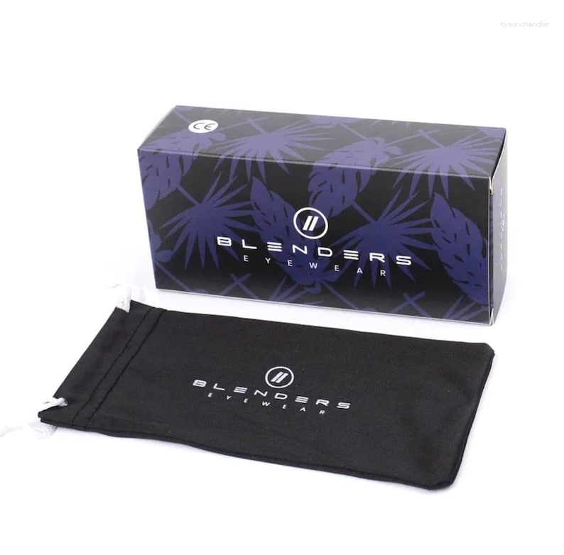 K&ouml;nnte beinhalten: Eine schwarze Schachtel mit einem blau-wei&szlig;en Bl&auml;ttermuster und dem Text "BLENDERS EYEWEAR". Ein schwarzer Kordelzugbeutel mit demselben Logo befindet sich neben der Schachtel. Die Schachtel hat ein CE-Zeichen.