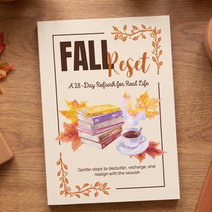 May include: A softcover book titled FALL Reset: A 28-Day Refresh for Real Life. The cover features a stack of colorful books, three lit candles, a teacup, and autumn leaves. The text reads: Gentle steps to declutter, recharge, and realign with the season.