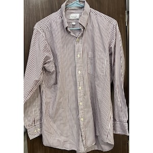 May include: A long-sleeved button-down shirt with vertical stripes in white and burgundy. The shirt has a button-down collar, a chest pocket, and buttoned cuffs. The shirt is hanging on a blue hanger.