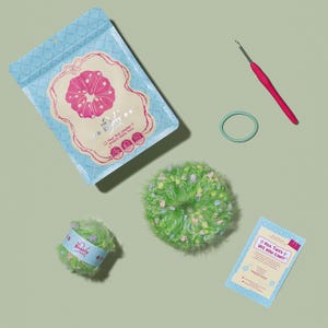 May include: A crochet kit with a green and pink scrunchie, a ball of green yarn, a crochet hook, a hair tie, and a card that says "Pick Twist YES YOU CAN!!" The kit comes in a blue bag with a pink scrunchie design.