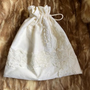 May include: A white drawstring bag with a lace trim and a button closure. The bag is made of a soft, lightweight fabric and is perfect for storing small items.