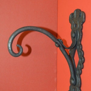 May include: A black metal wall-mounted hook with a decorative scroll design. The hook has a curved arm that extends out from the wall.