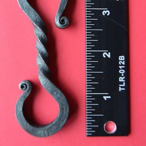 May include: A twisted metal hook with a rounded end. The hook is about 3 inches long and is shown next to a ruler.