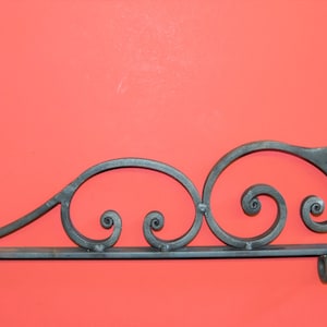 May include: Black metal sign bracket with a decorative scroll design. The bracket has three hooks on the bottom.
