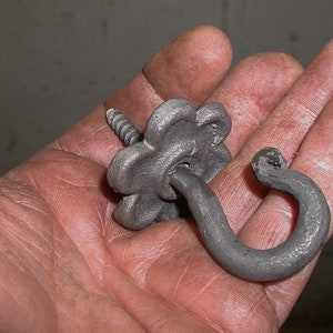 May include: A black metal hook with a decorative flower-shaped base. The hook is attached to a screw.