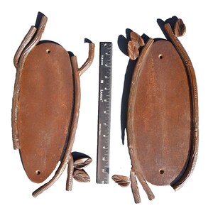 May include: Two rustic metal oval-shaped plaques with a twig and leaf design. The plaques are brown and have a rough texture.