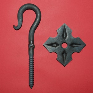 May include: A black metal hook with a screw thread and a decorative cross-shaped plate. The hook has a rounded top and a pointed bottom.