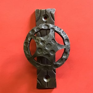 May include: A black metal door knocker with a star-shaped design. The knocker is attached to a rectangular plate with two decorative holes.