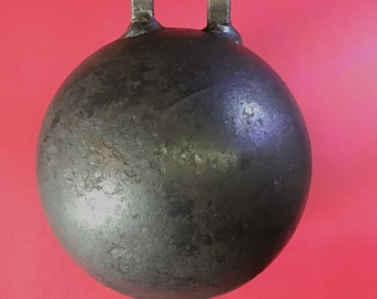 May include: A dark, metallic gray kettlebell with a rounded body and a handle. The kettlebell is set against a red background. A black ruler is at the bottom of the image.