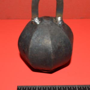 May include: A black metal weight with a handle. The weight is shaped like a sphere with a textured surface. The handle is a simple loop.