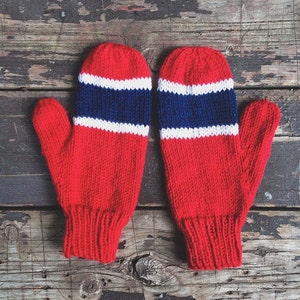May include: A pair of red knitted mittens with white and blue stripes. The mittens are on a wooden surface.