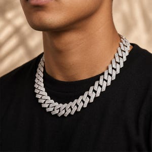 May include: A silver-toned cuban link chain necklace featuring a dense pavé setting of small, clear, reflective stones covering the entire surface of each interlocking rectangular link, worn around the neck against a plain black t-shirt.