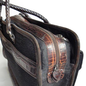 May include: A black leather briefcase with a brown alligator-embossed trim and a zipper closure. The briefcase has a top handle and a shoulder strap.