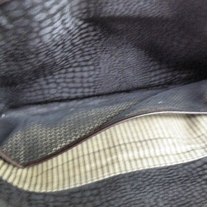 May include: The inside of a brown leather bag with a black fabric lining and a small pocket. The fabric lining has a striped pattern.