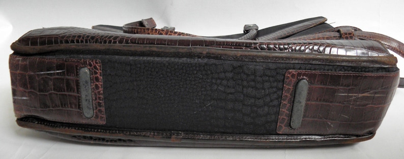 May include: A brown leather briefcase with a crocodile pattern. The briefcase has a black fabric lining and a zipper closure.