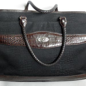 May include: A black canvas tote bag with brown leather trim and a braided handle. The bag has a crocodile-embossed design and a silver metal accent.