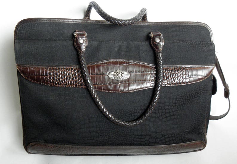 May include: A black canvas tote bag with brown leather trim and a braided handle. The bag has a crocodile-embossed design and a silver metal accent.