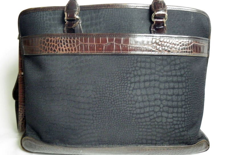 May include: A black leather tote bag with a crocodile embossed pattern. The bag has two top handles and a brown leather trim.