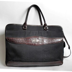 May include: A black leather briefcase with a brown crocodile embossed trim and a silver buckle. The bag has a top handle and a detachable shoulder strap.