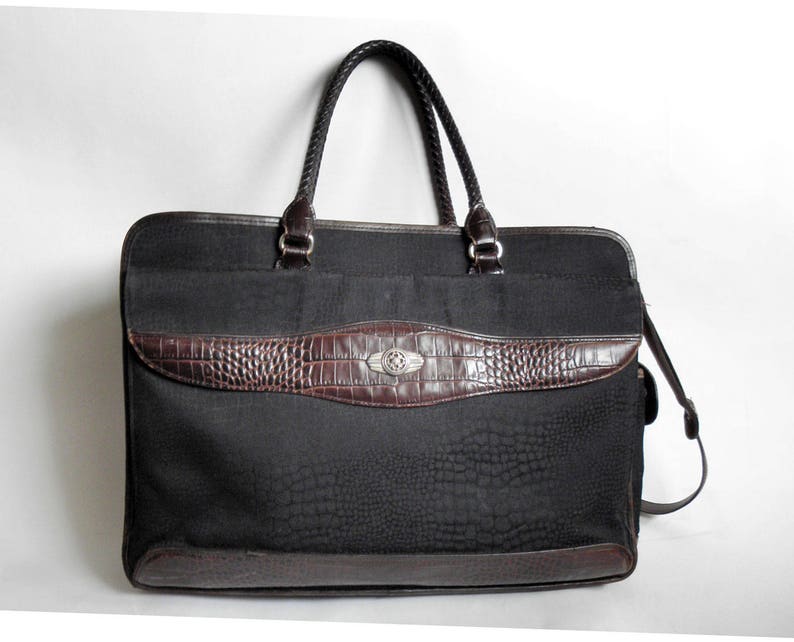 May include: A black leather briefcase with a brown crocodile embossed trim and a silver buckle. The bag has a top handle and a detachable shoulder strap.