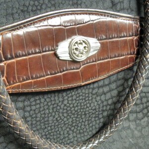 May include: A black leather handbag with a brown crocodile embossed flap and a silver metal accent. The bag has a braided strap.