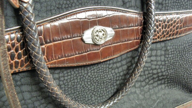 May include: A black leather handbag with a brown crocodile embossed flap and a silver metal accent. The bag has a braided strap.