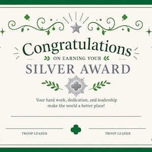 May include: A certificate with a white background and a green border. The text "Congratulations on Earning Your Silver Award" is displayed in the center. Decorative elements include stars, shamrocks, and flourishes. The bottom of the certificate has lines for troop leader signatures.